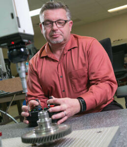 Man with remote control in front of cylinder-shape metal part.
